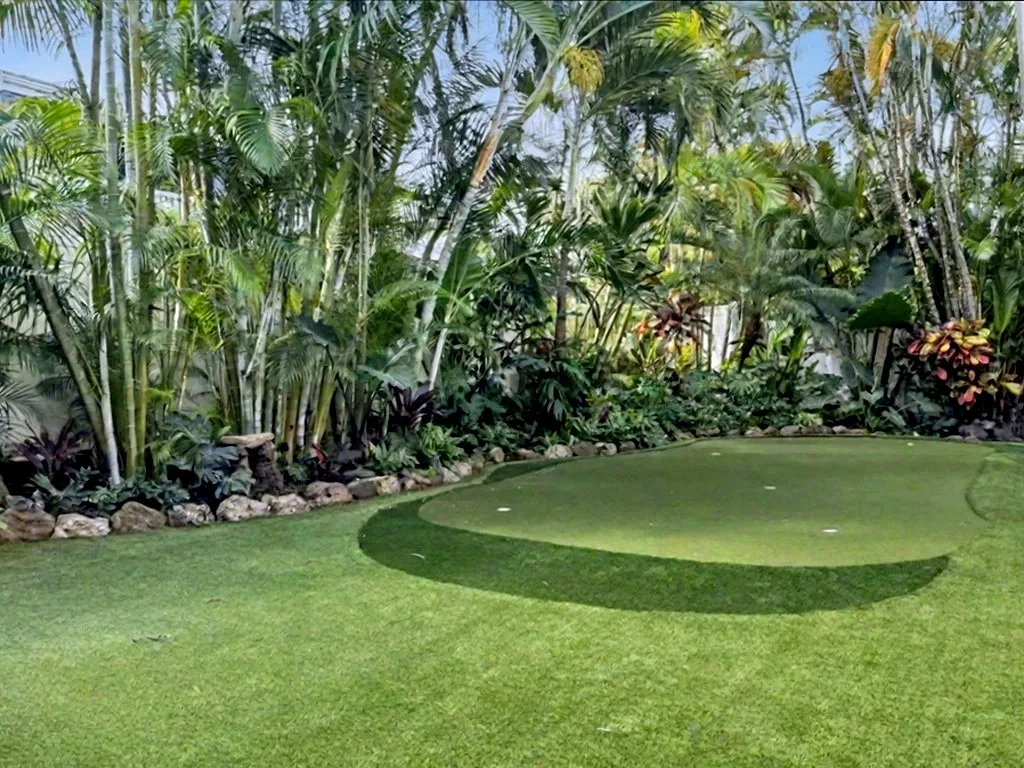 A landscaped lawn bordered by tropical plants and palm trees.