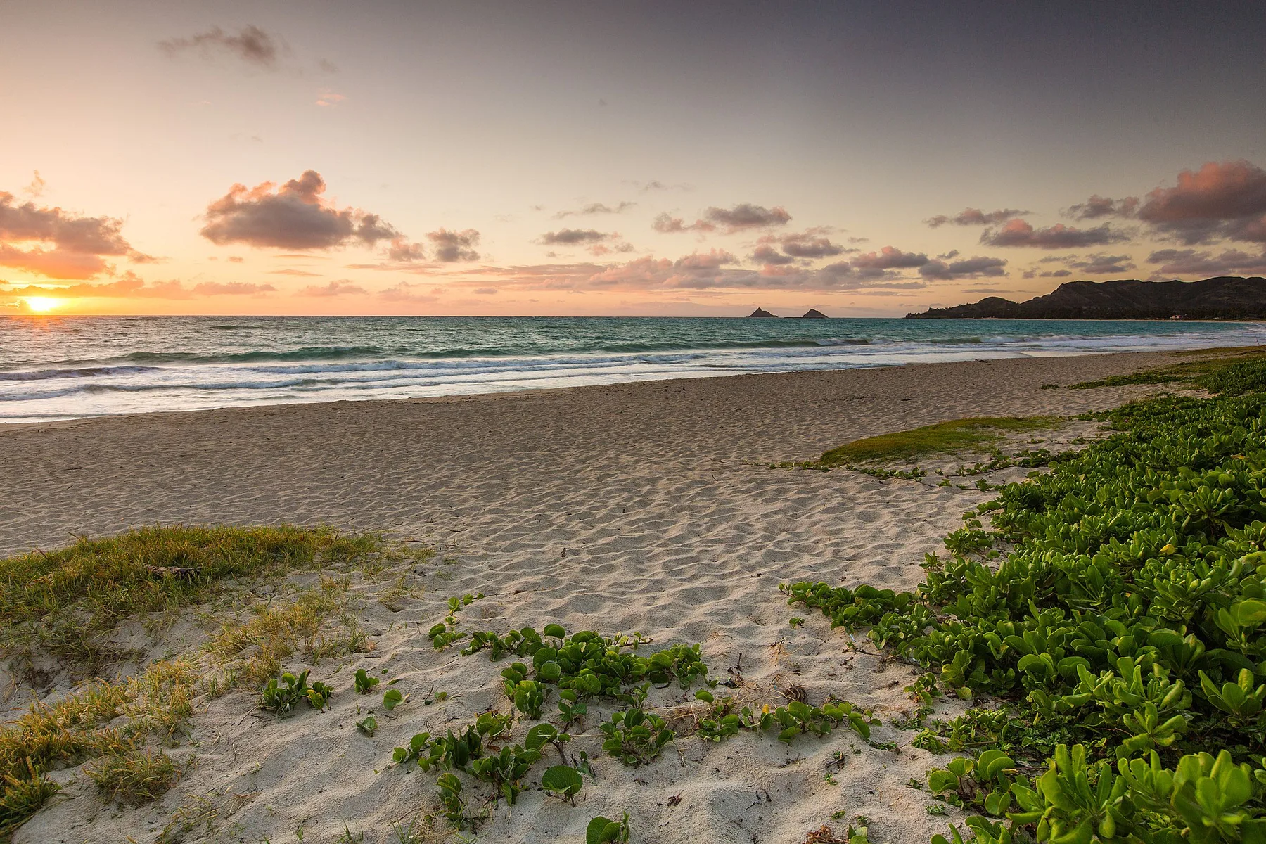 A sandy beach meets the ocean beneath a colorful sunset sky.