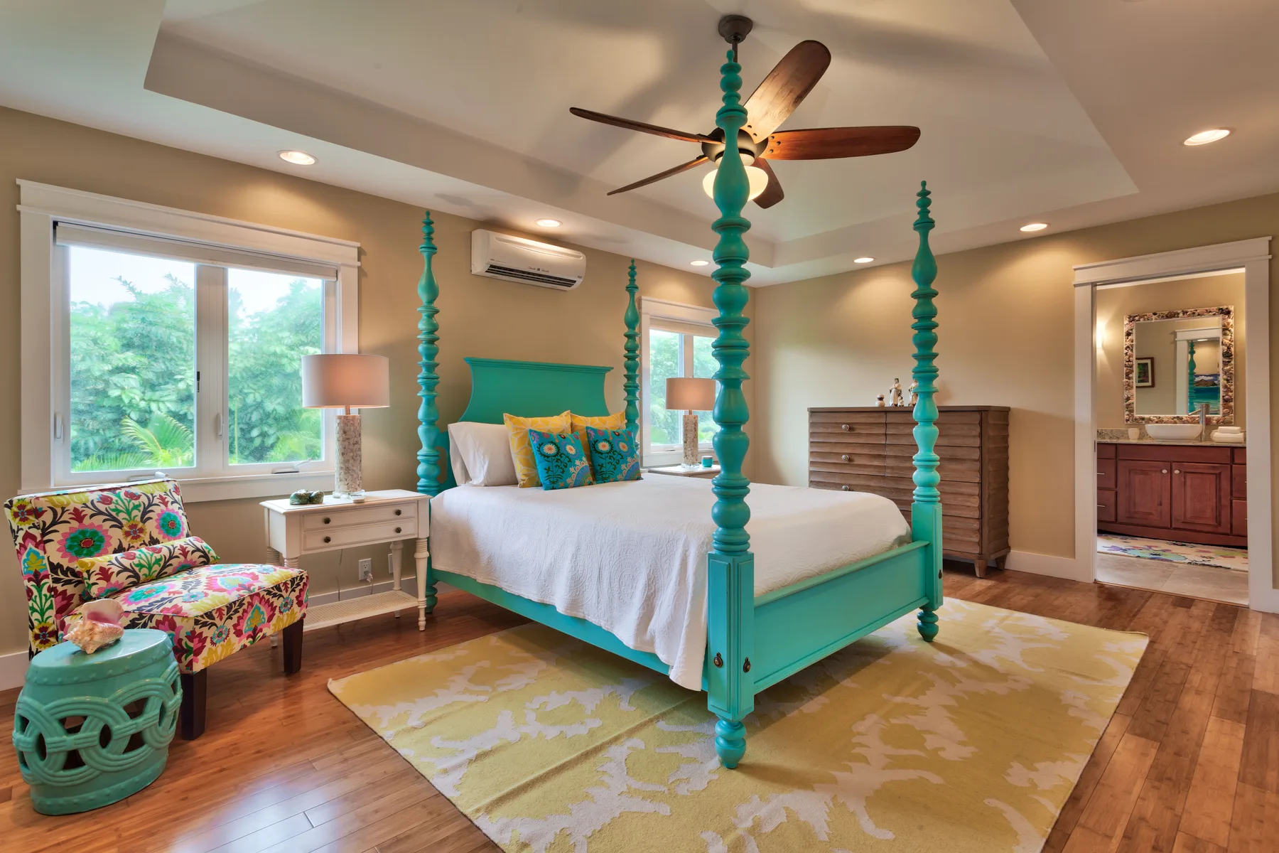 A bedroom with a turquoise bed, colorful seating, and a ceiling fan.