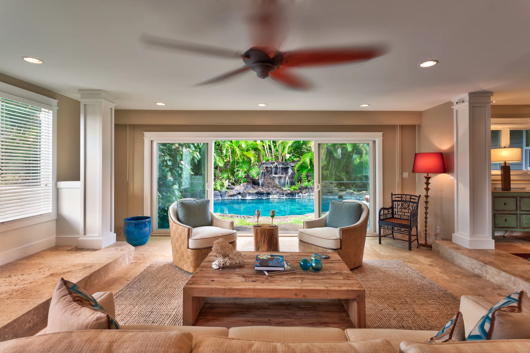 A bright living room opens onto a patio with a swimming pool and lush greenery.