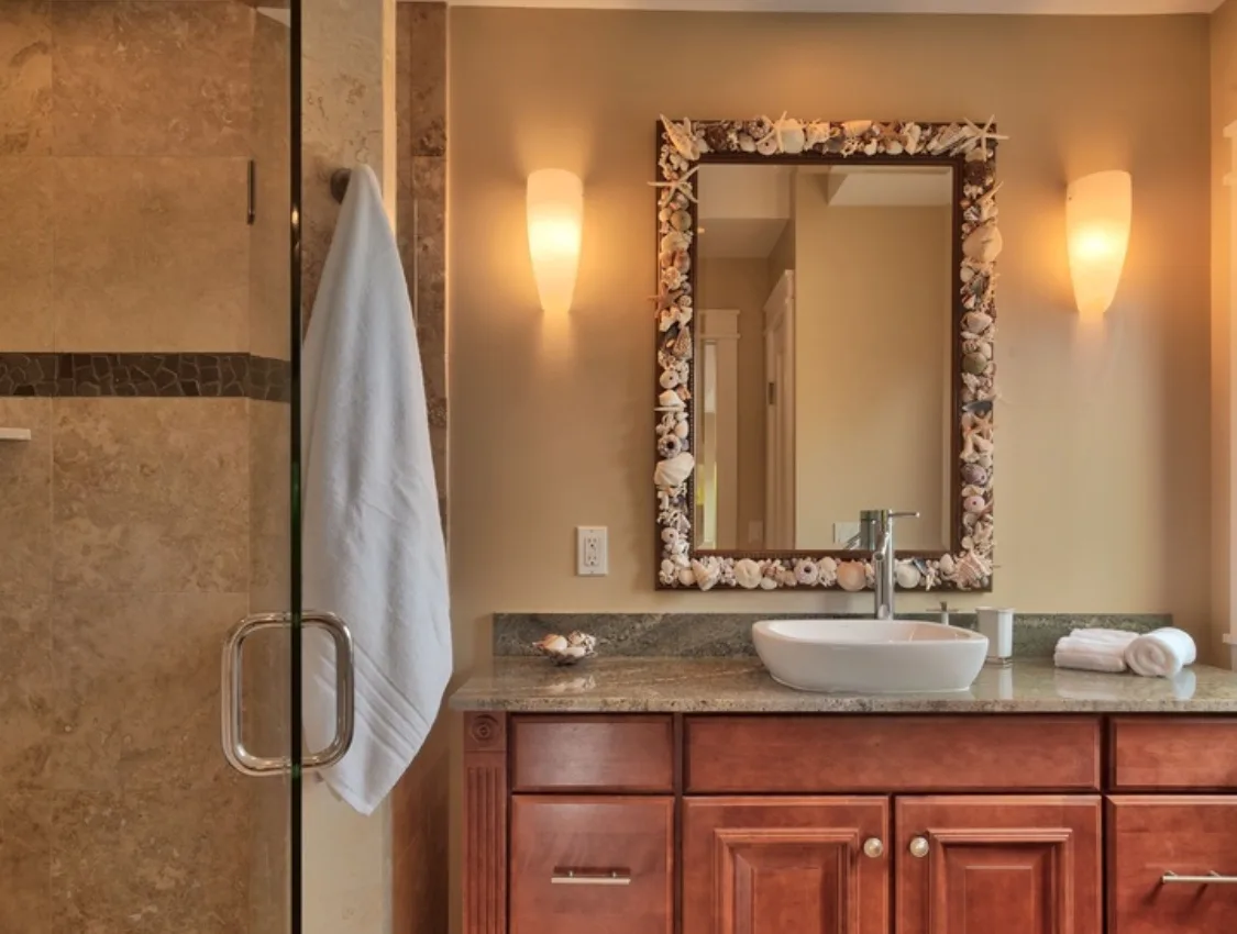A bathroom vanity with a framed mirror and a towel beside the shower.