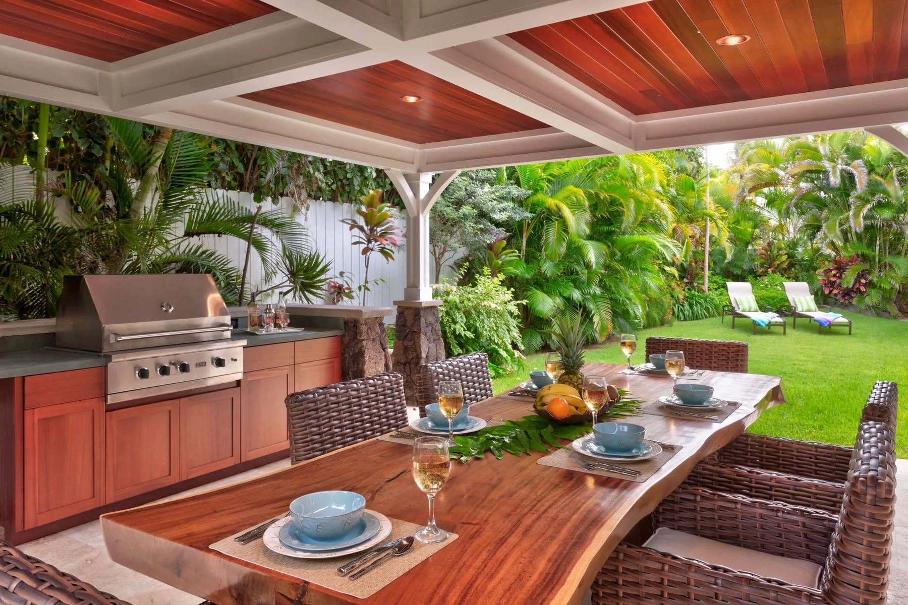 A covered outdoor dining area with a long table beside a garden.
