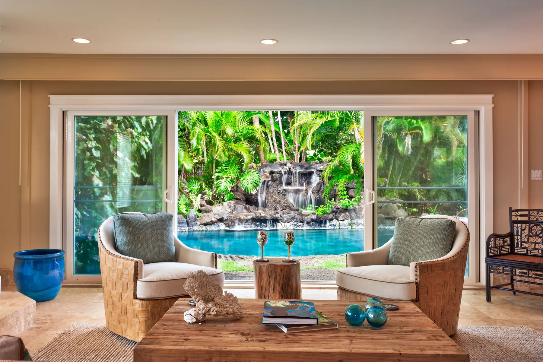 A living room seating area overlooks a turquoise pool and tropical waterfall.