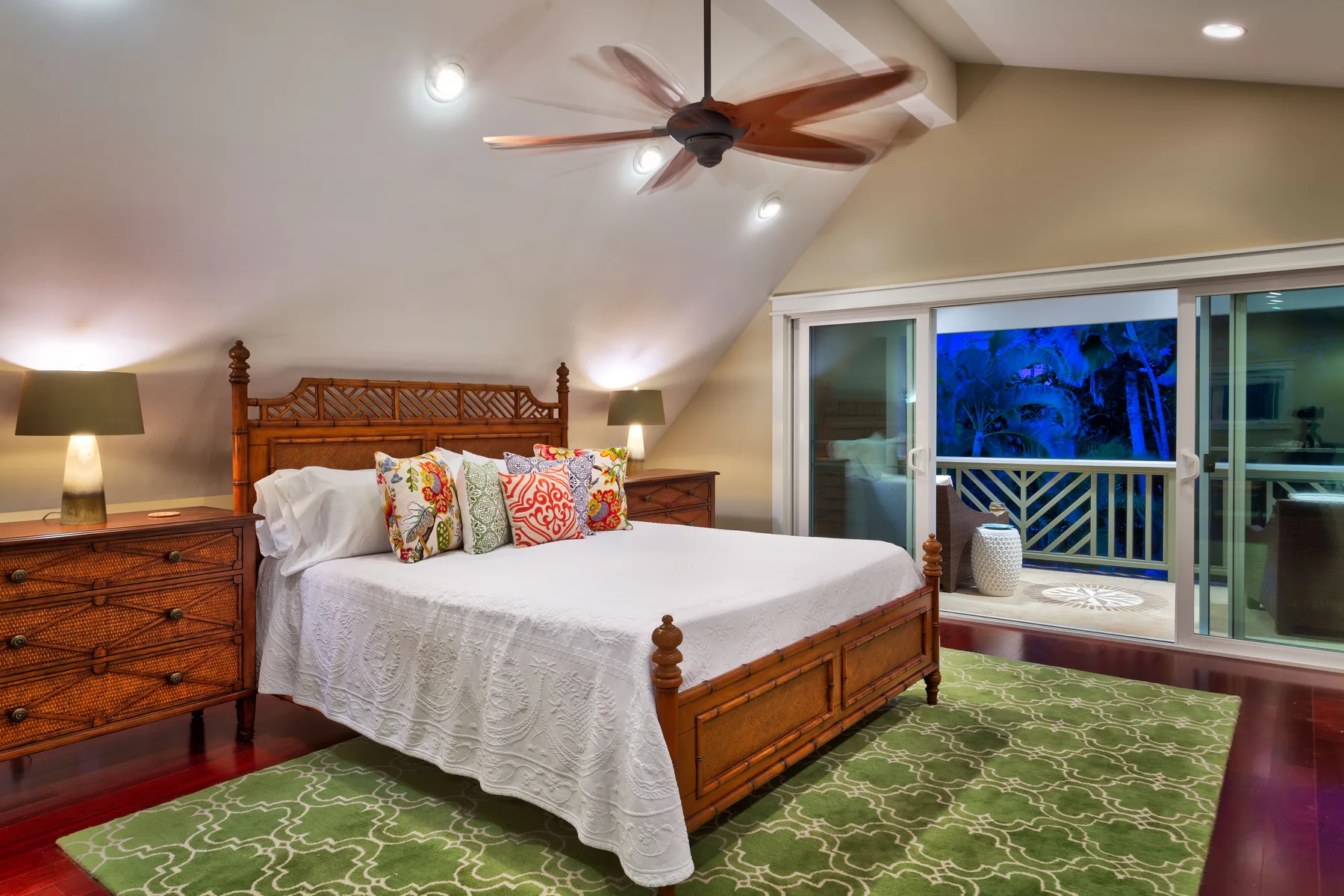 A bedroom with a wooden bed, patterned rug, and sliding glass doors opening to a balcony.