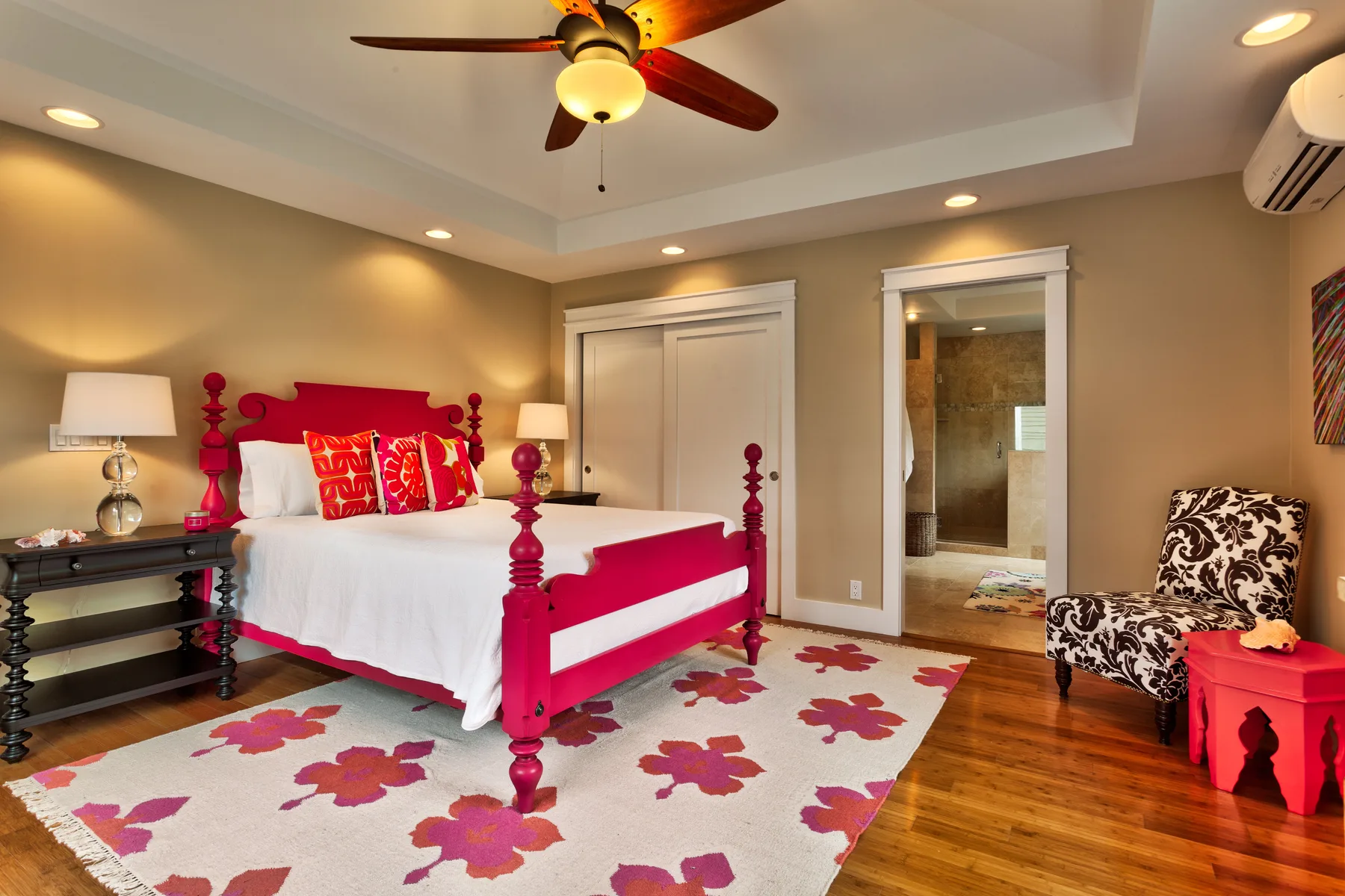 A bedroom with a red bed, floral rug, and an open bathroom doorway.