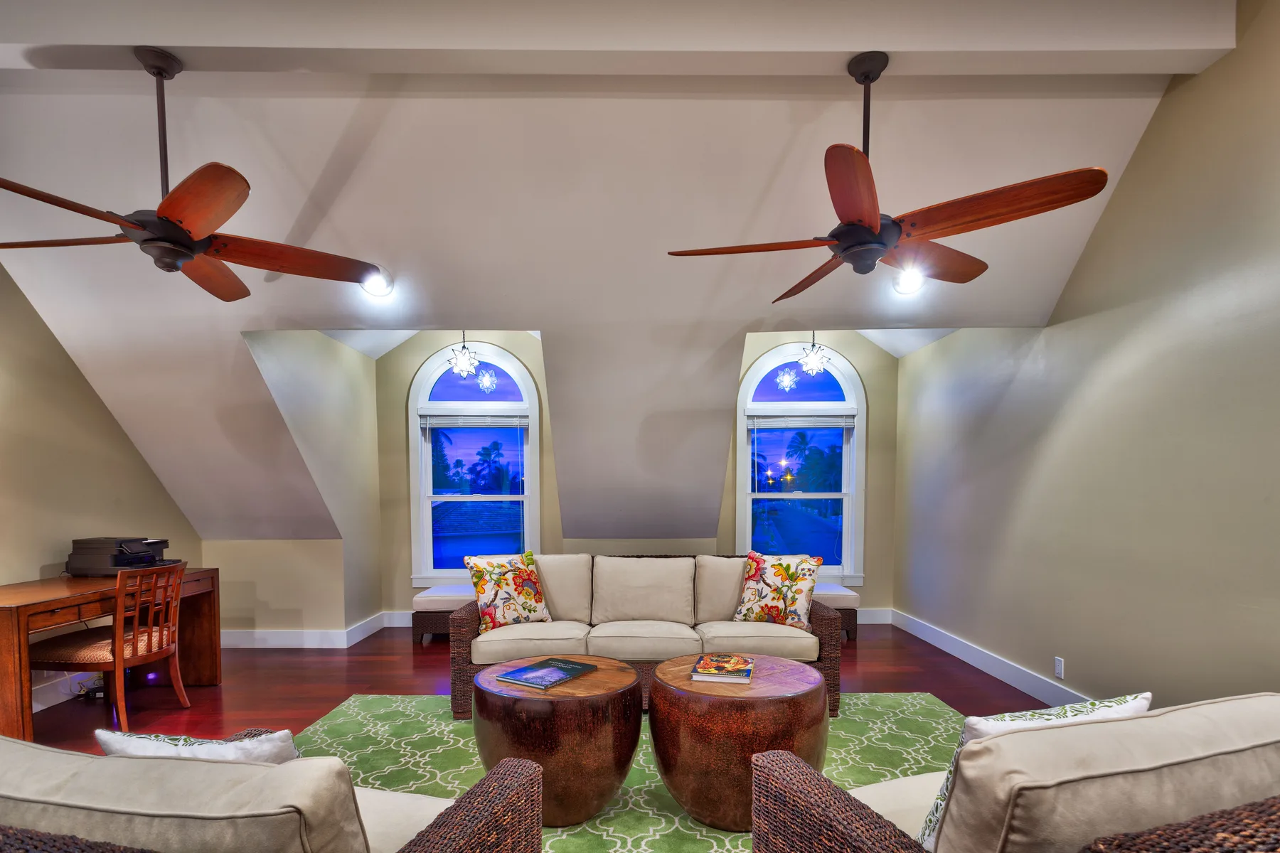 A living room with seating around two low tables and windows along the back wall.