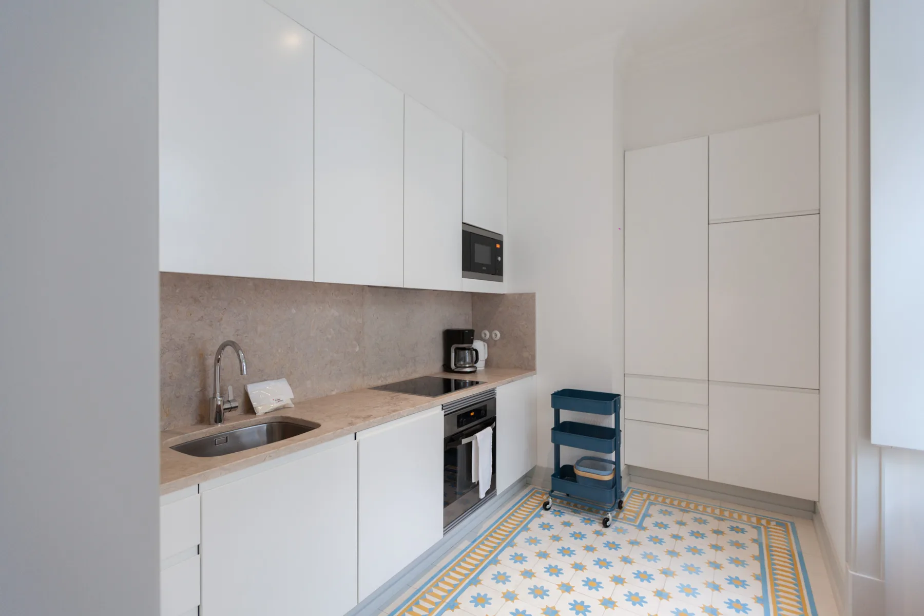 Una cocina luminosa con armarios blancos y un suelo estampado.