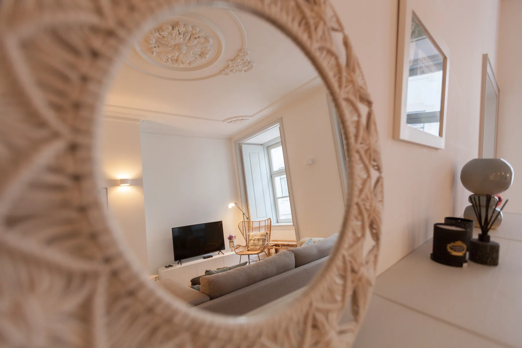Una sala de estar reflejada en un espejo ornamentado, con asientos y un televisor.