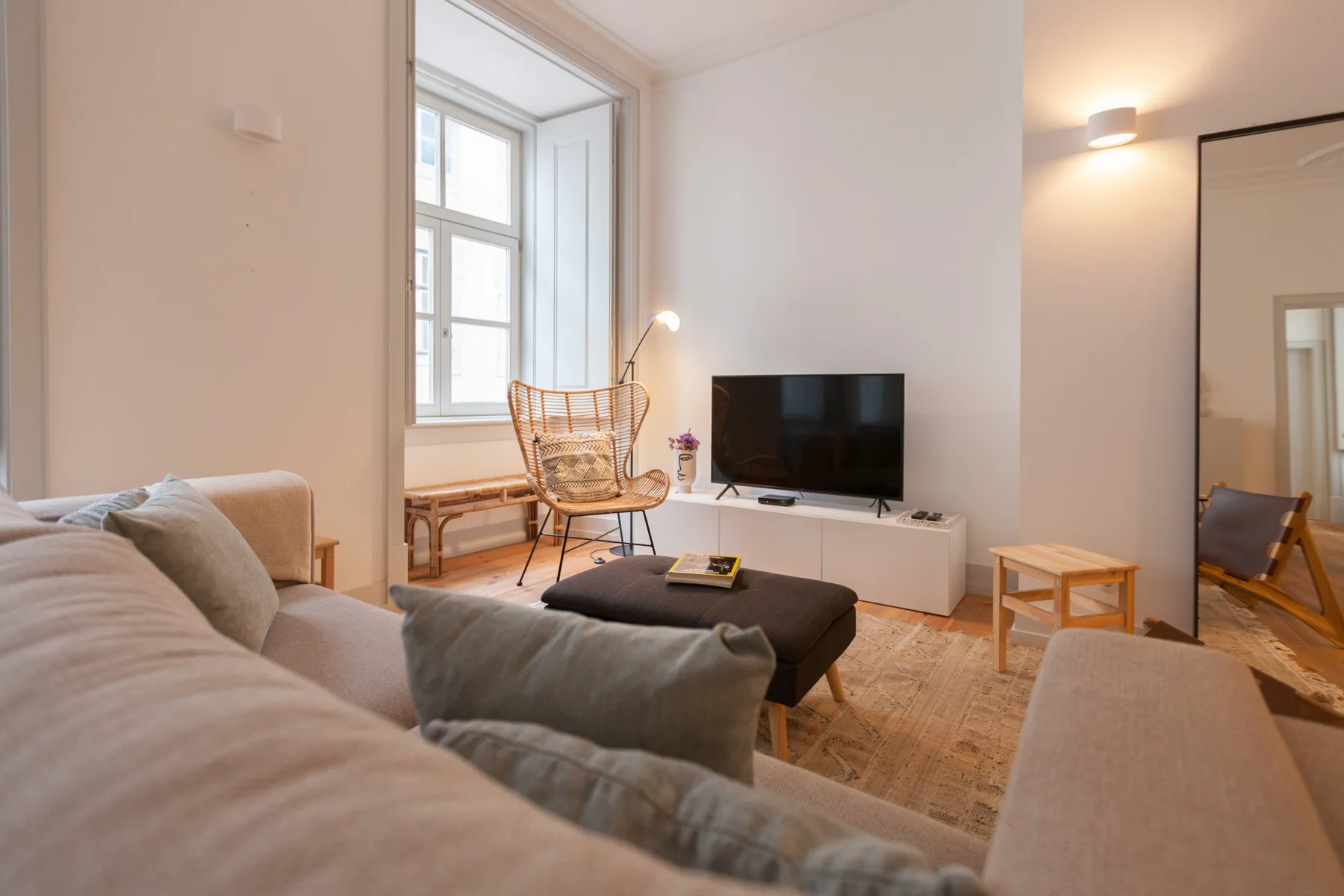 Una sala de estar con asientos, un televisor y una ventana alta.