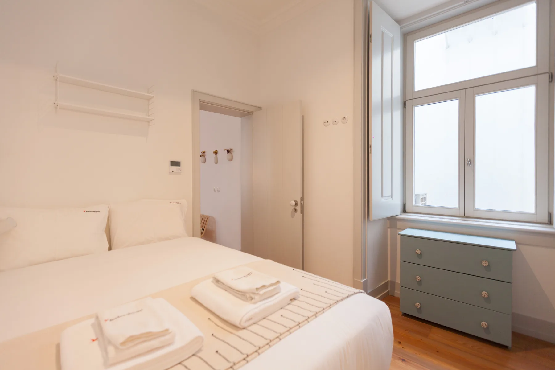 Un dormitorio luminoso con una cama bien tendida junto a una ventana grande.