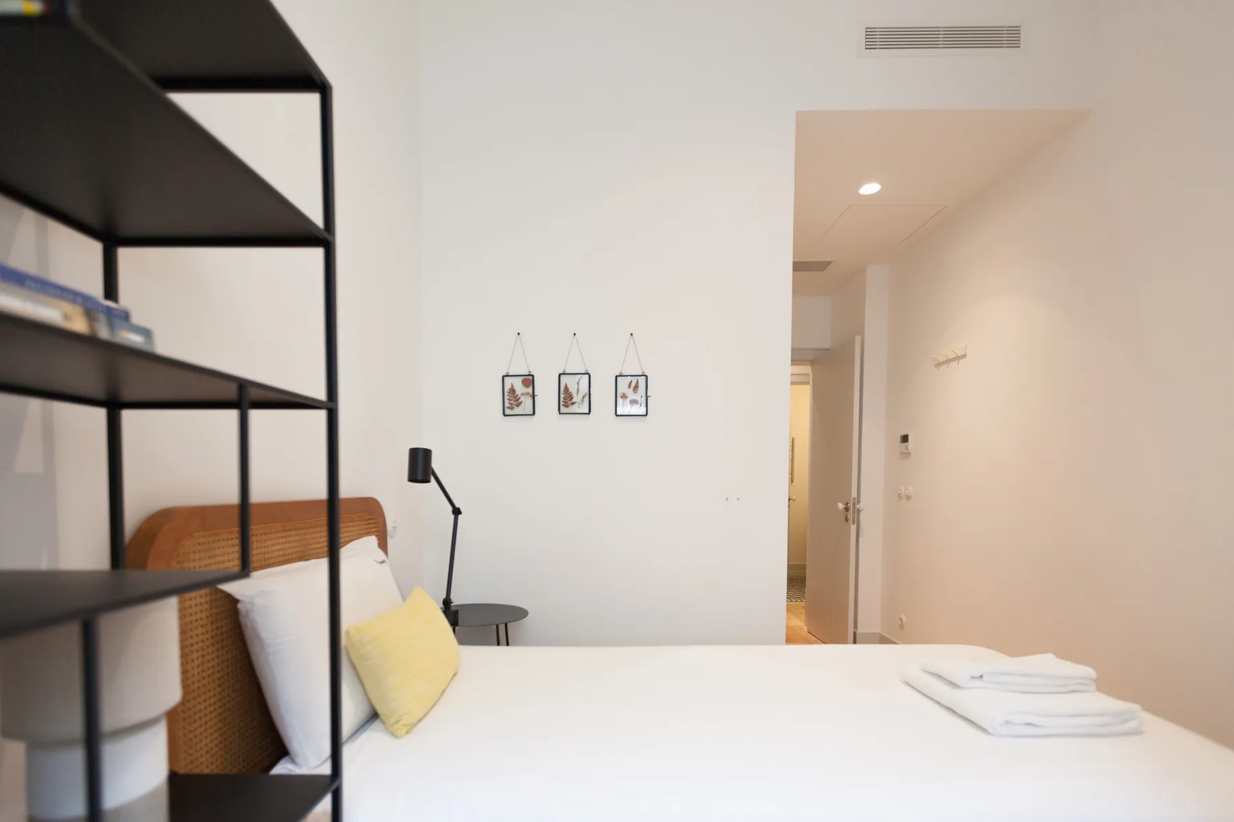 Un dormitorio luminoso con una cama, una mesita de noche y estanterías abiertas.