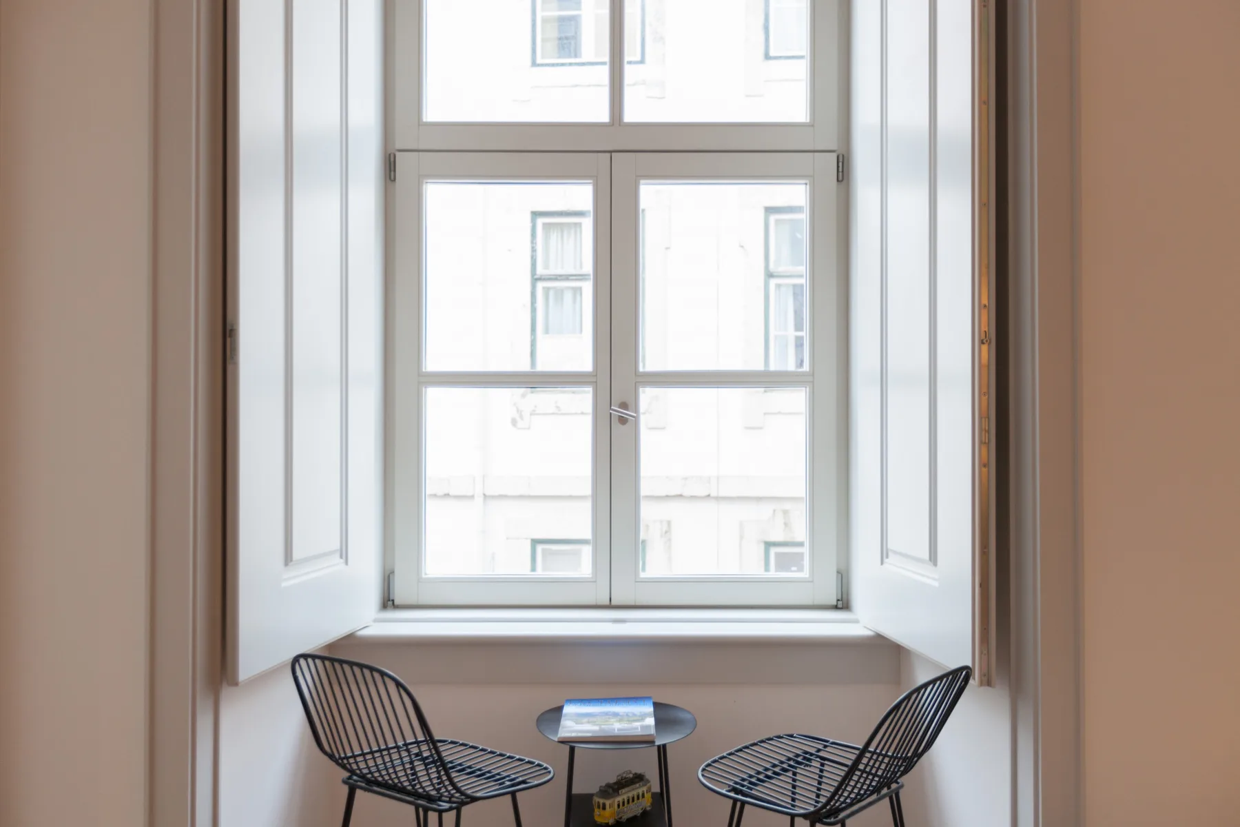 Una zona de estar junto a una ventana grande, con dos sillas y una mesa pequeña.