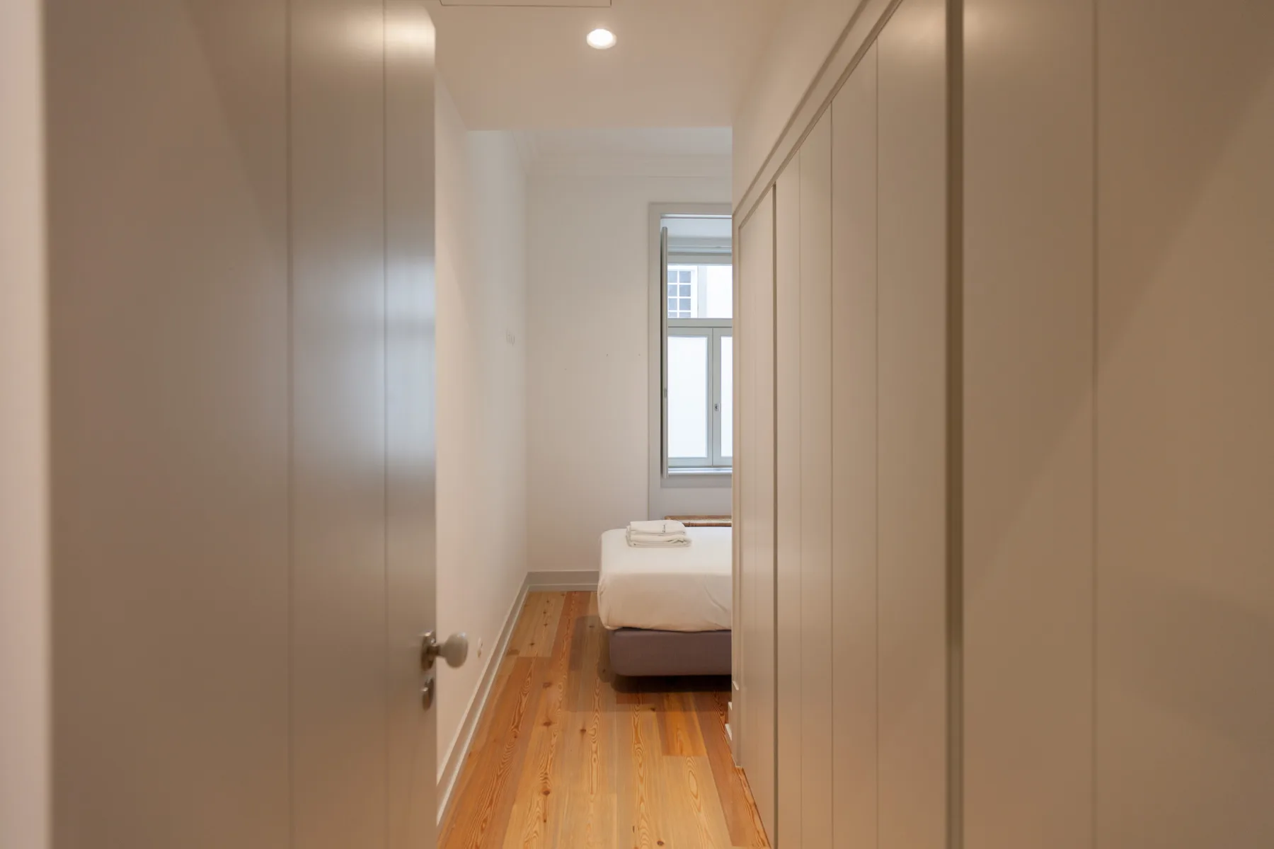 Un dormitorio con una cama y una ventana al final de un pasillo estrecho.