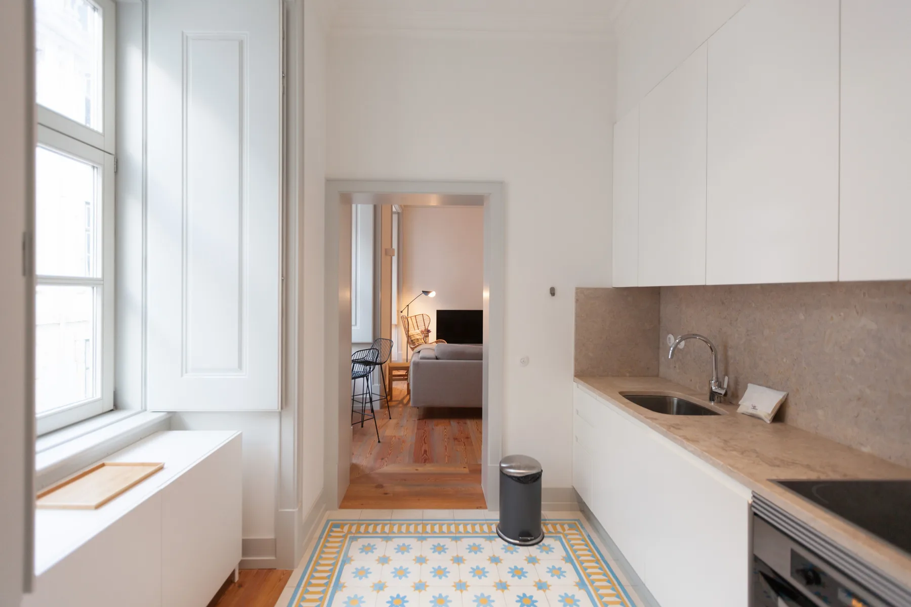 Una cocina luminosa con una alfombra estampada y vista a la sala de estar.