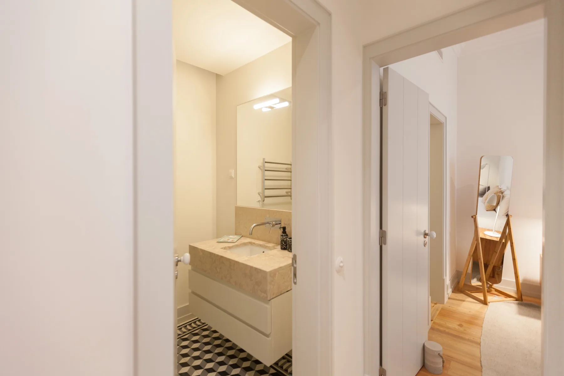 Un baño con lavabo da a un pasillo con un espejo.