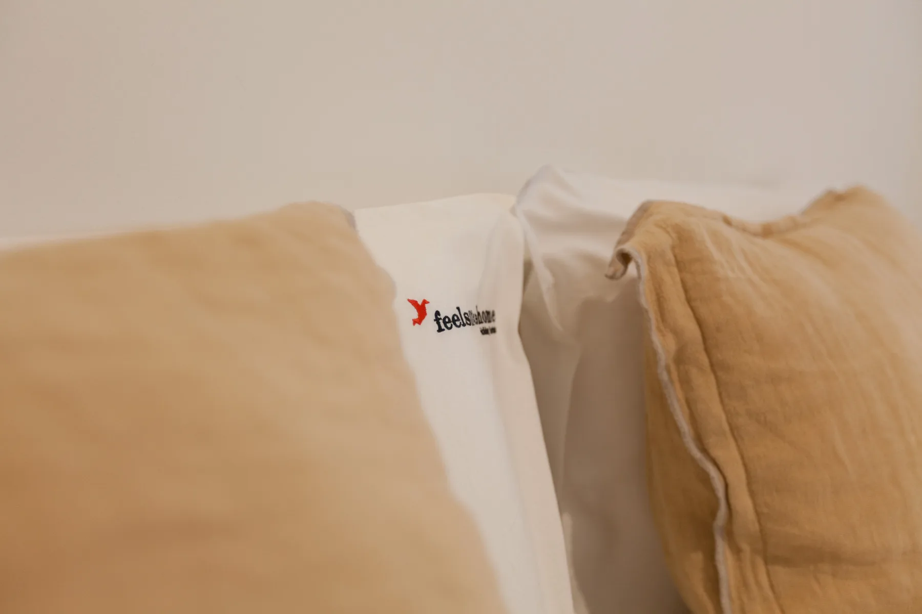 Una cama con sábanas blancas y almohadas color tostado.