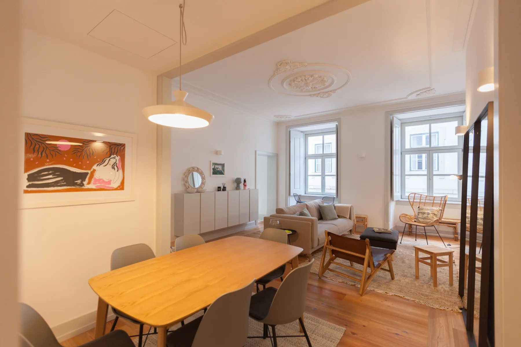Zona de comedor y sala de estar con una mesa, asientos y ventanas altas.