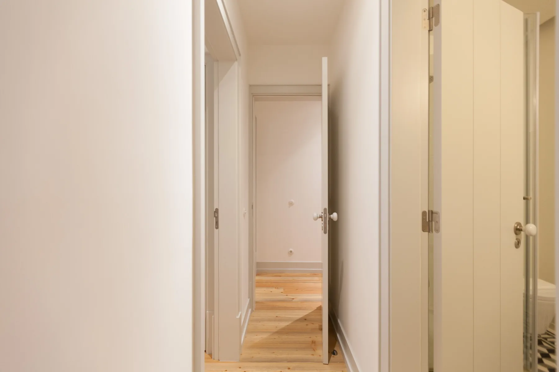Un pasillo estrecho con puertas abiertas y suelo de madera.