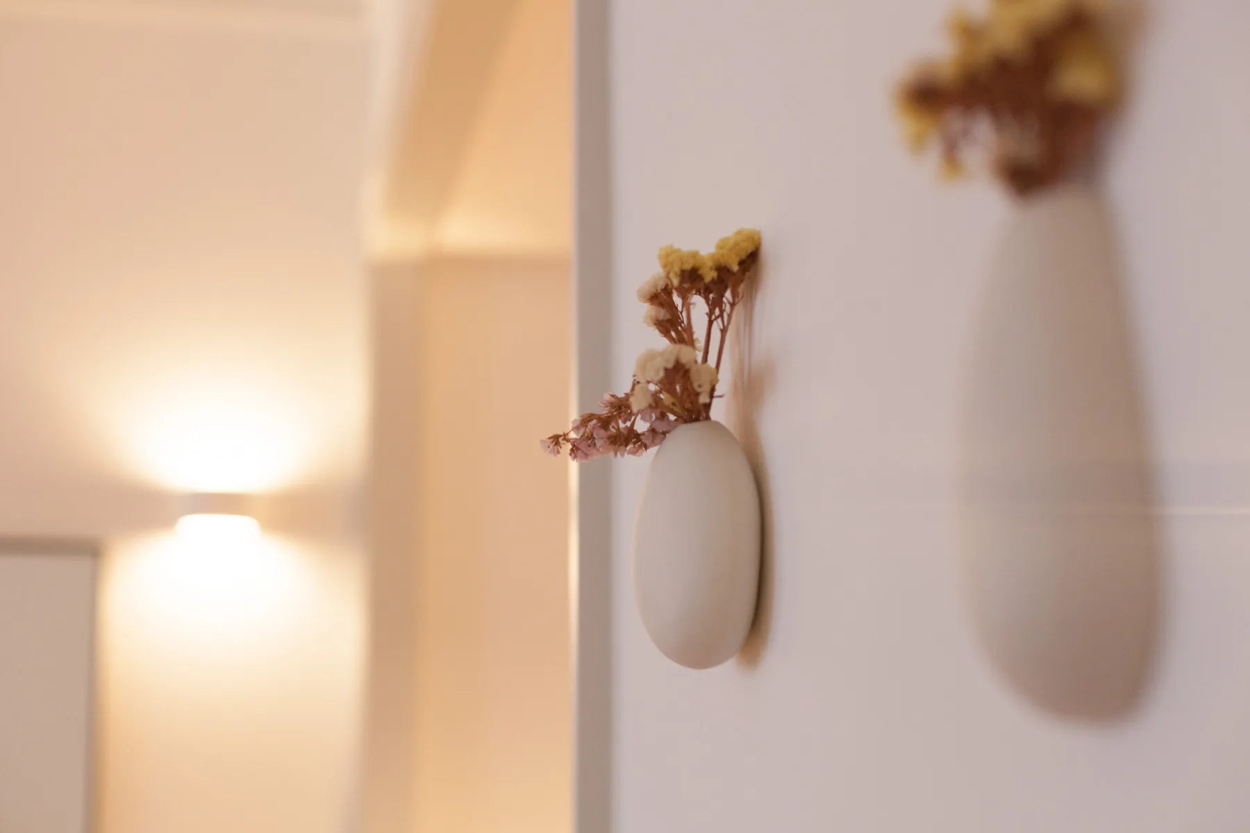 Una pared interior con luz tenue presenta un pequeño jarrón con flores secas.