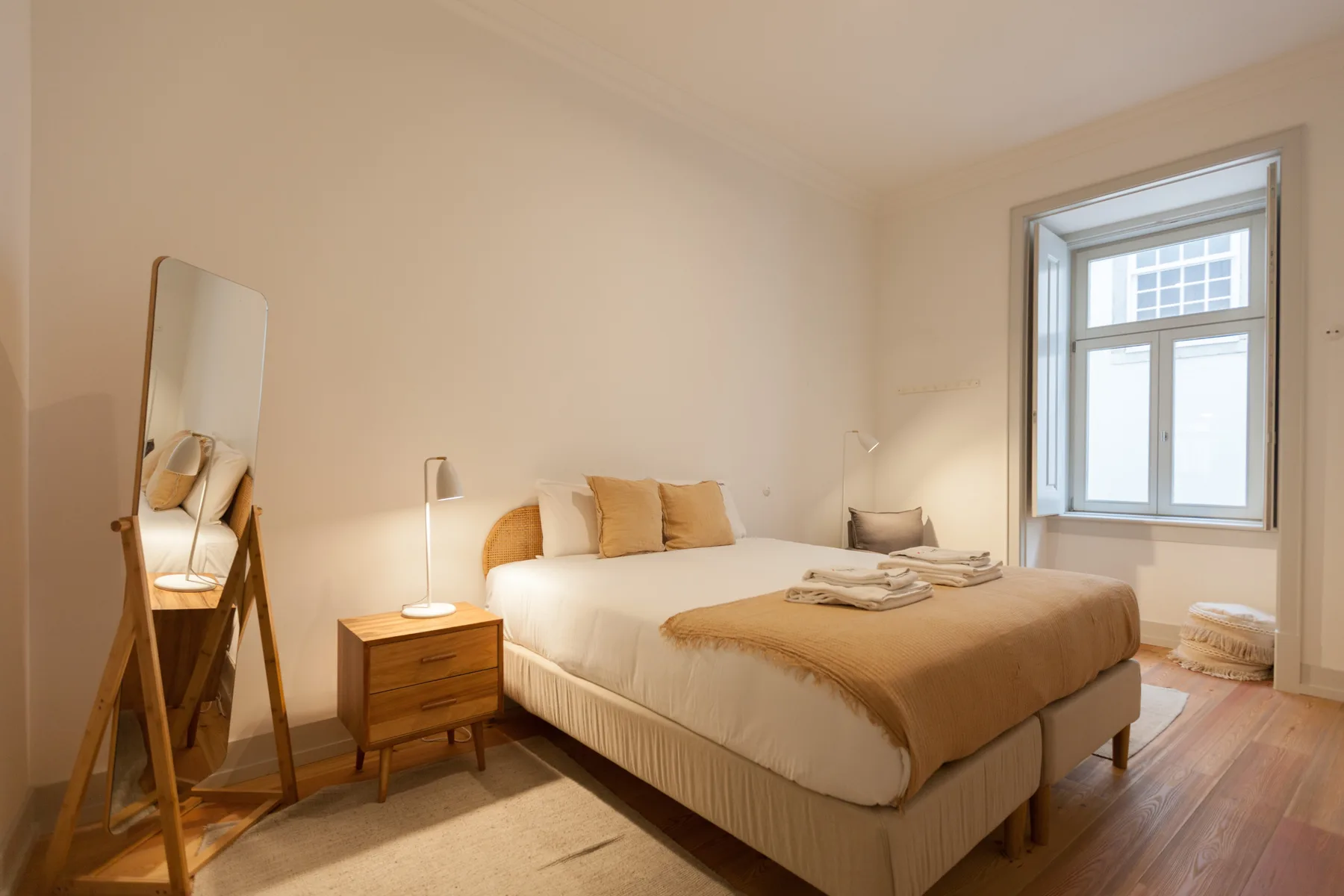 Dormitorio con una cama grande, una mesita de noche y un espejo alto.