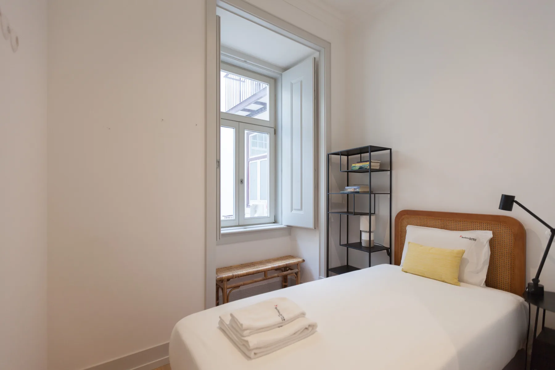 Un dormitorio con una cama, toallas dobladas y una ventana alta.
