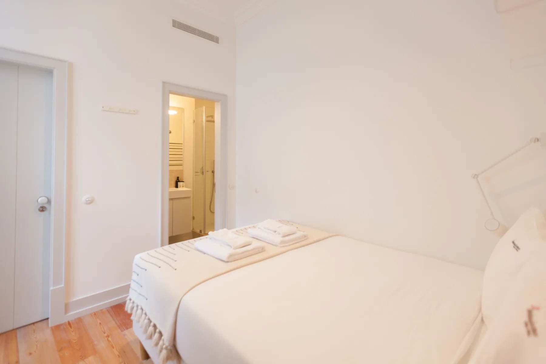 Un dormitorio luminoso con una cama bien arreglada y una puerta abierta al baño.