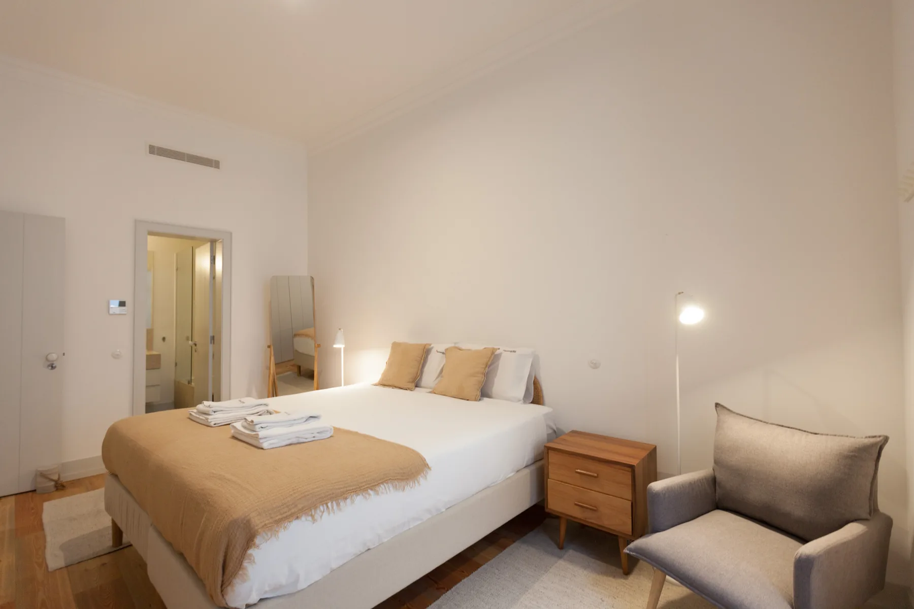 Un dormitorio luminoso con una cama y un sillón tapizado al lado.