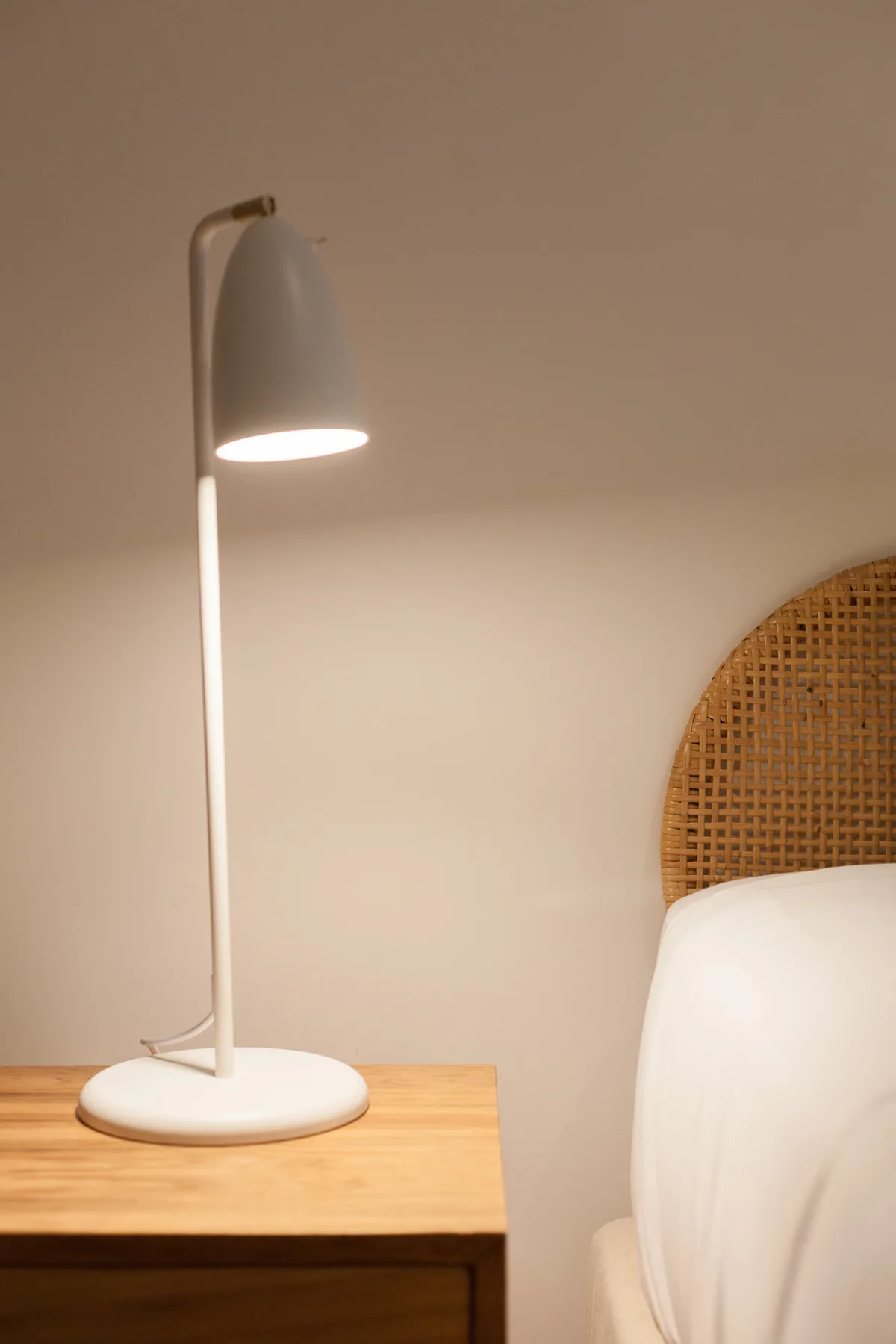 Una lámpara de noche está sobre una mesa de madera junto a una cama.