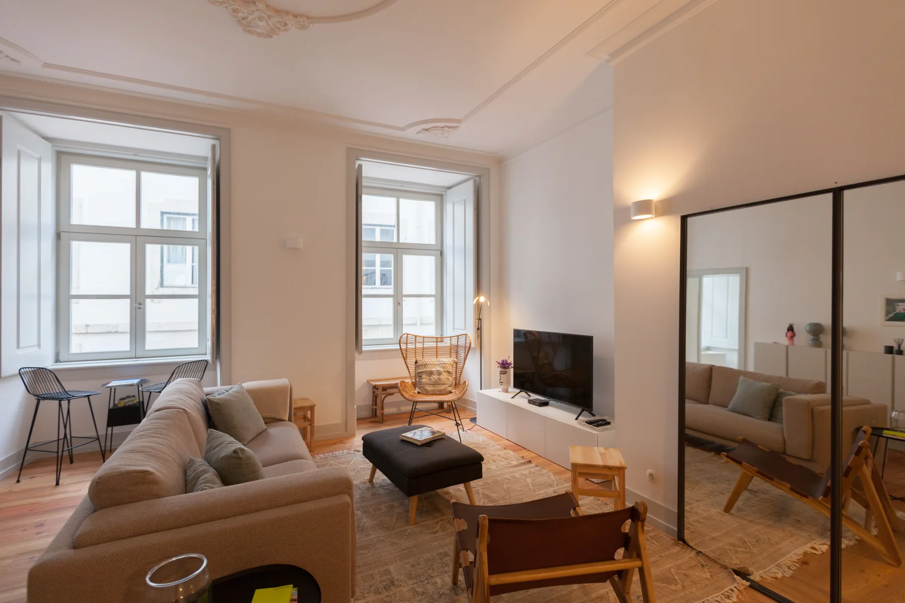 Una sala luminosa tiene asientos, un televisor y ventanas altas.