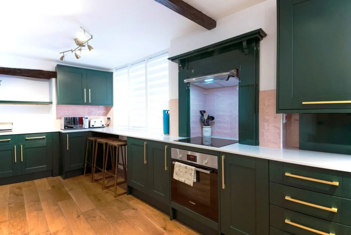 Una cocina con gabinetes verde oscuro y un horno bajo la encimera.