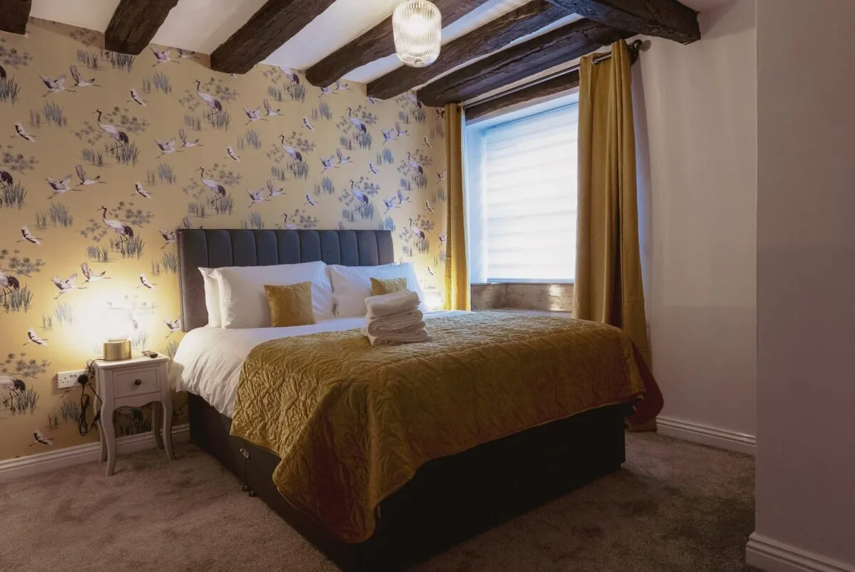 Un dormitorio con una cama grande, papel pintado estampado y una ventana con cortinas.