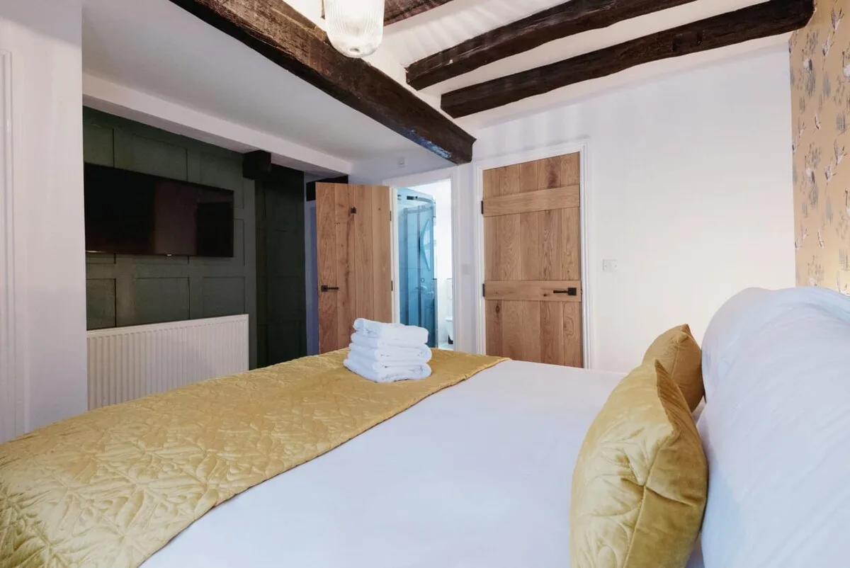 Un dormitorio con una cama blanca y toallas dobladas bajo vigas oscuras de madera.