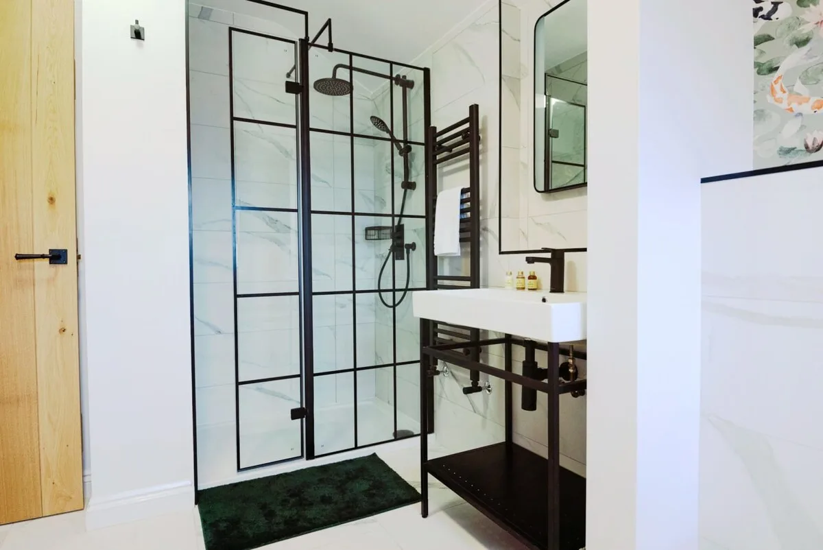 Un baño con una ducha de vidrio y un lavabo sobre un soporte metálico oscuro.