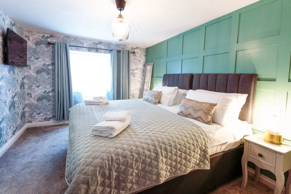 Un dormitorio con una cama grande, ropa de cama en capas y una pared verde con paneles.