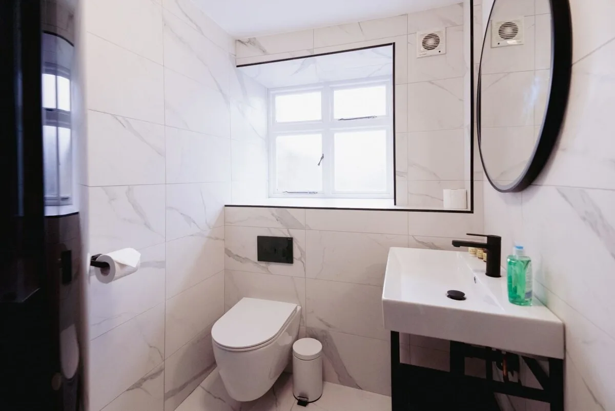 Un baño alicatado con inodoro, lavabo y una ventana luminosa.