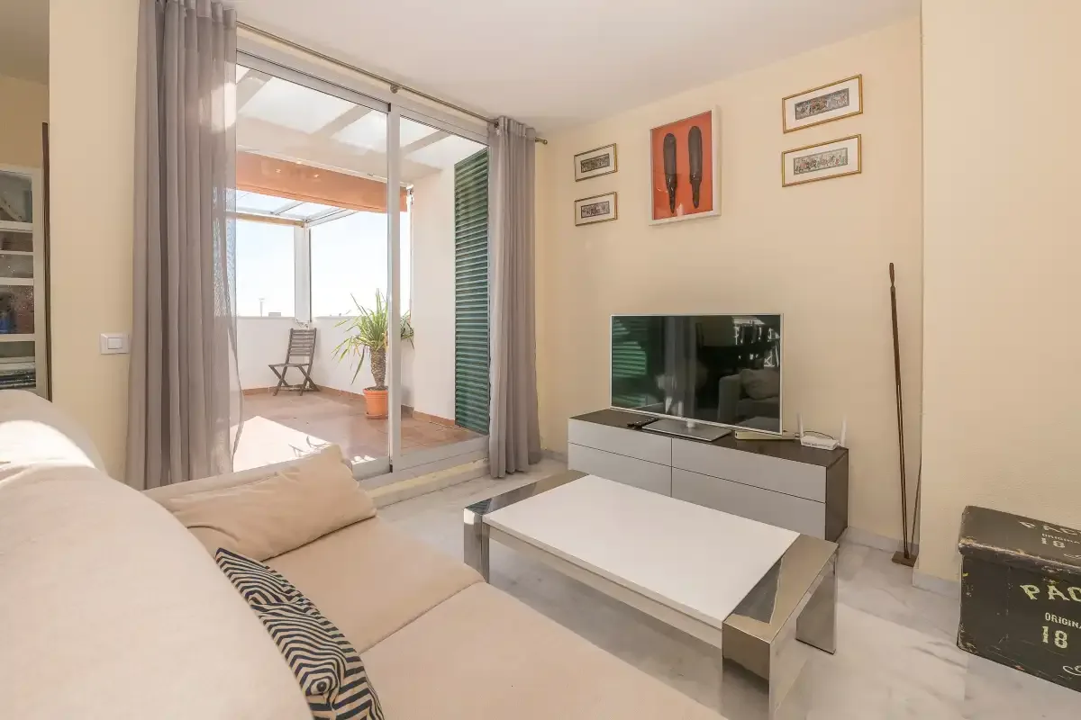 Una sala luminosa con asientos y un televisor junto a puertas de vidrio.
