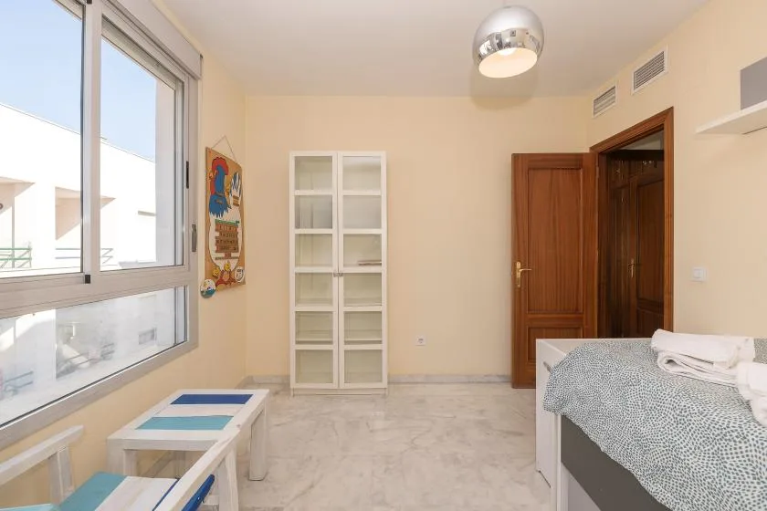 Un dormitorio con una cama, un armario alto y ventanas amplias.