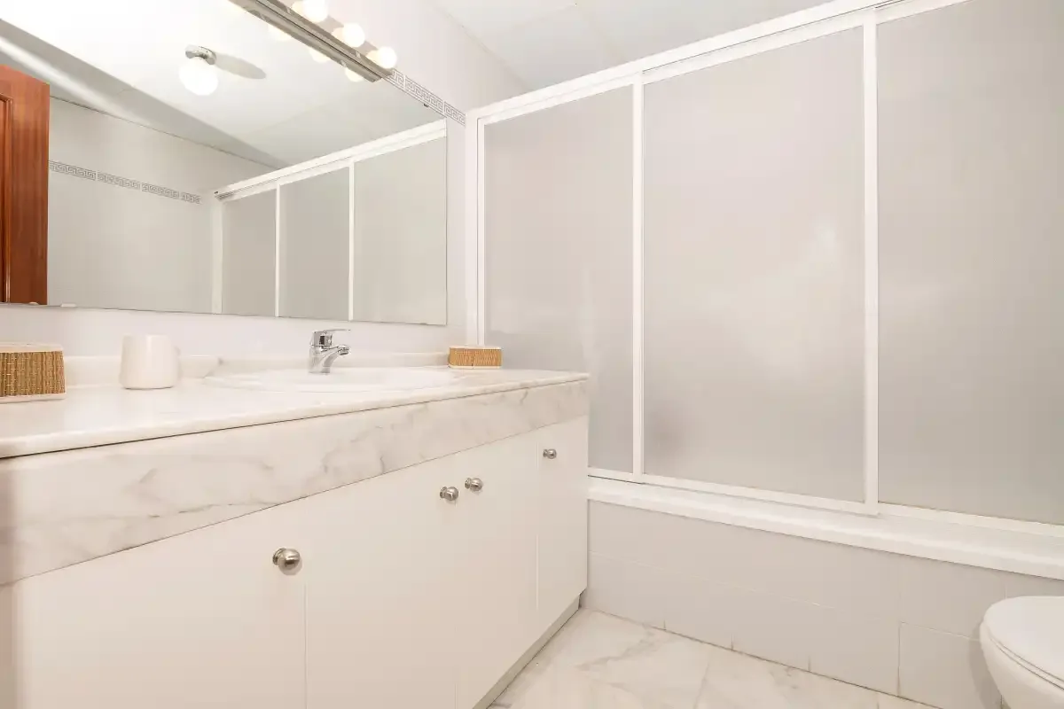 Un baño luminoso con un amplio lavabo, espejo y paneles de vidrio esmerilado.