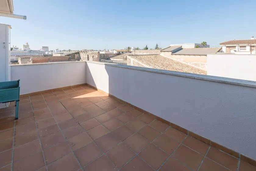 Una terraza soleada en la azotea con suelo de baldosas y muros bajos.