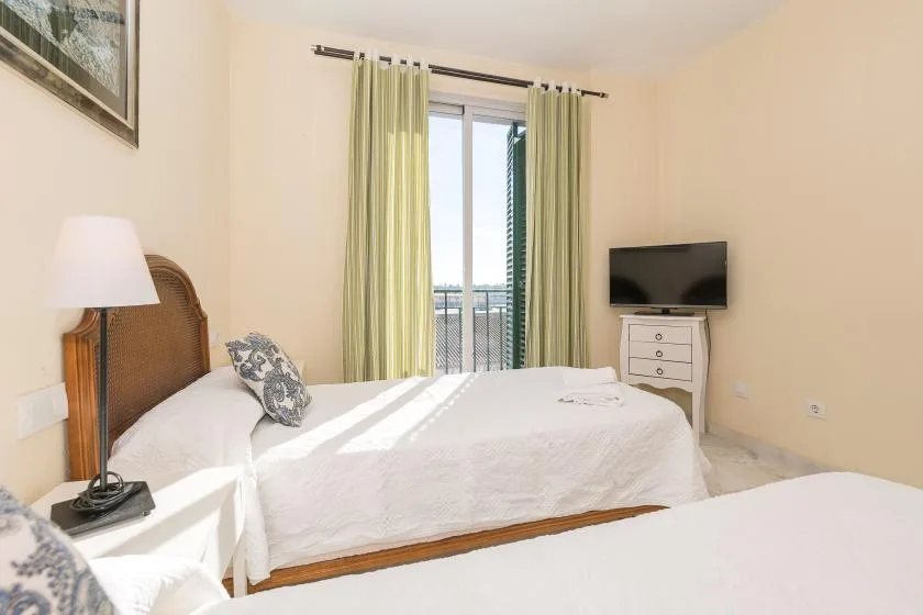 Un dormitorio con una cama junto a una puerta de cristal con cortinas y un televisor.