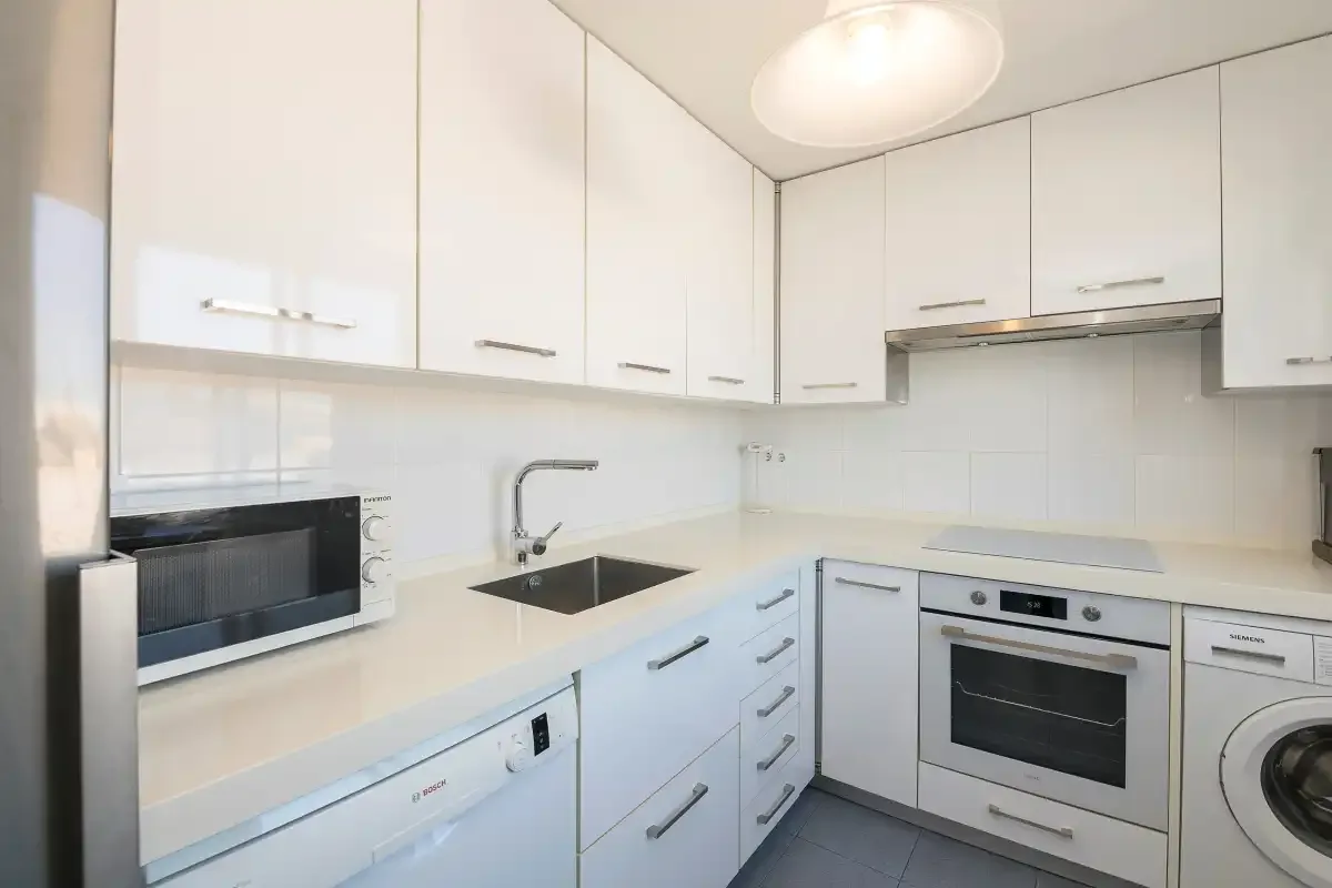 Una cocina luminosa con armarios blancos, una placa de cocción y electrodomésticos integrados.
