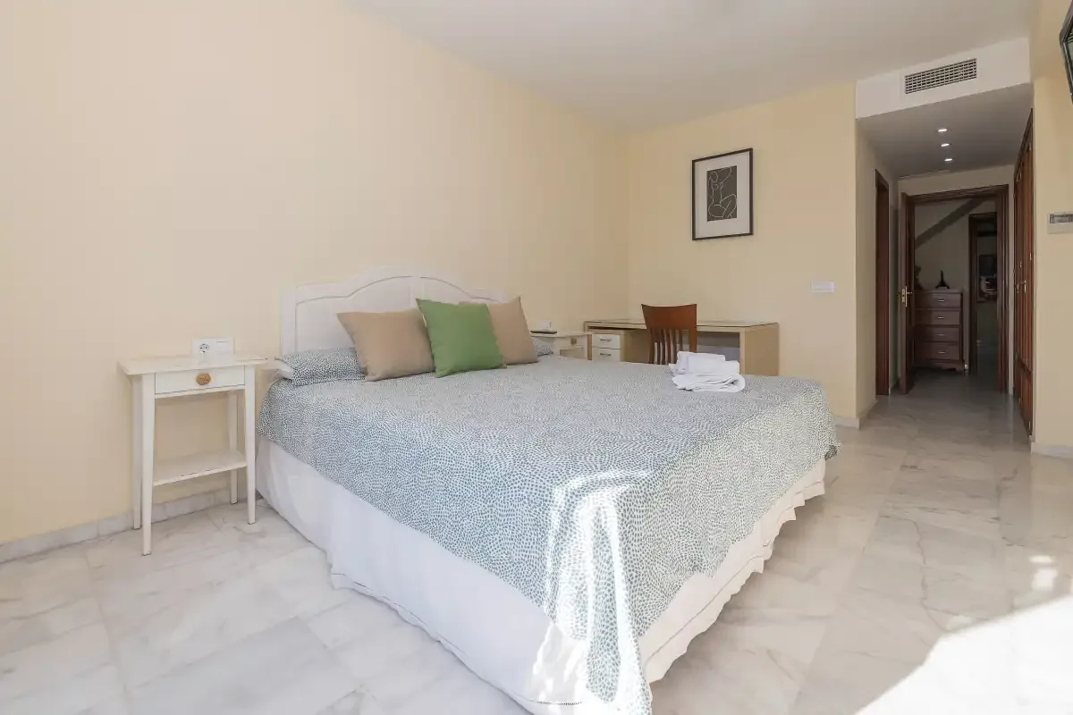 Un dormitorio con una cama bien hecha y una pequeña mesita de noche.