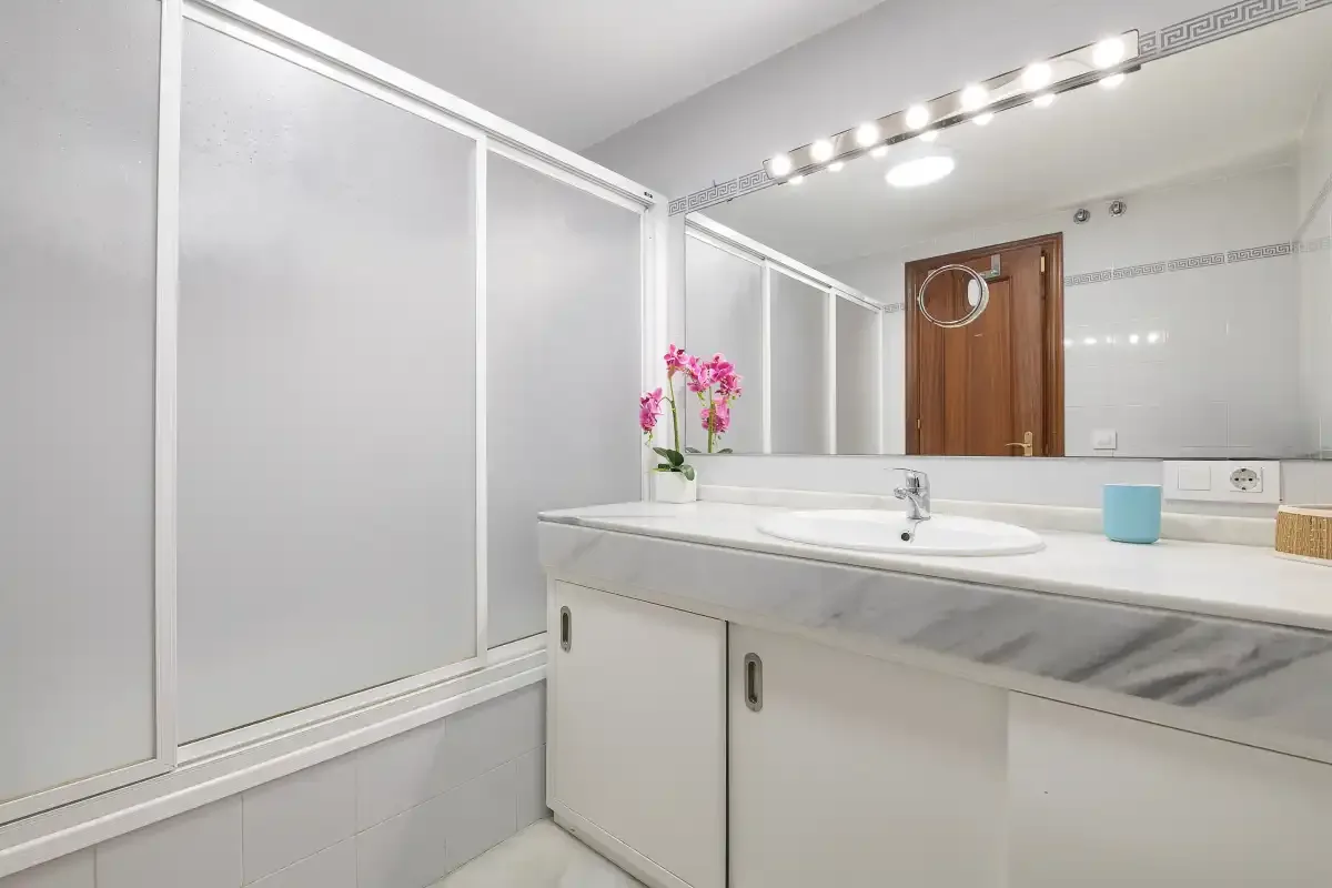 Un tocador de baño con un espejo amplio y paneles correderos de ducha.