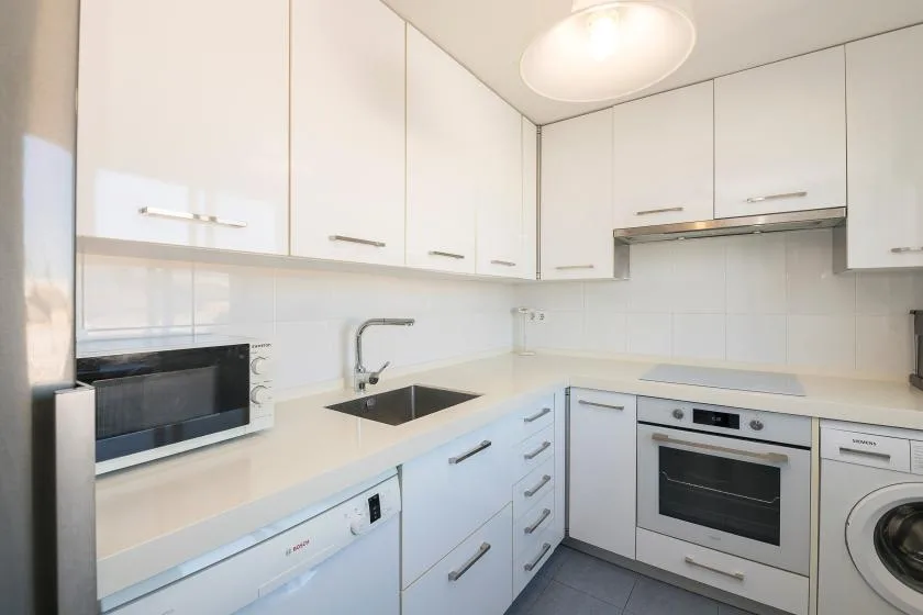 Una cocina moderna y luminosa con gabinetes blancos, placa de cocción y electrodomésticos integrados.