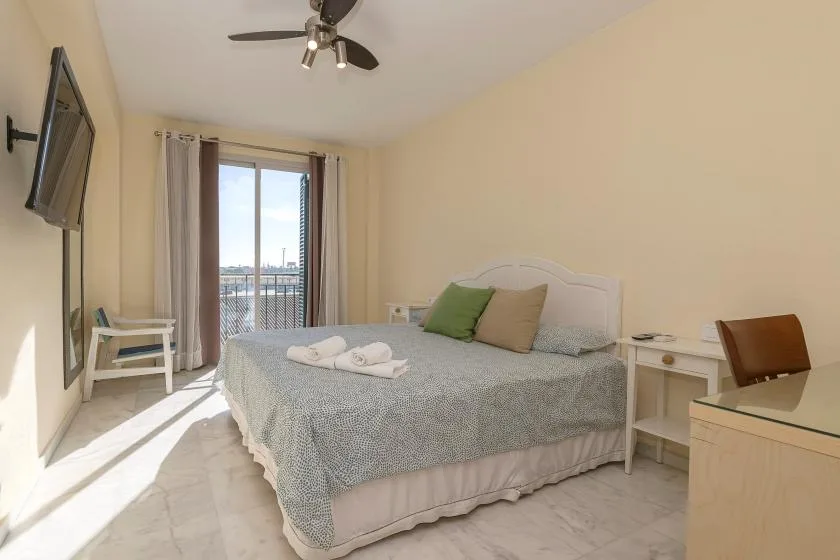 Un dormitorio luminoso con cama, mesita de noche y puertas al balcón.