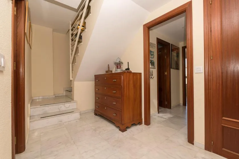 Un pasillo luminoso con una escalera, peldaños de mármol y una cómoda de madera.