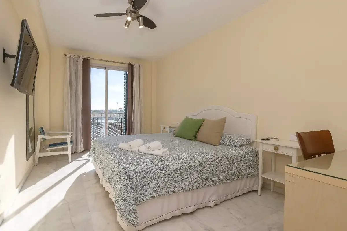 Un dormitorio con una cama, mesitas de noche y una puerta de cristal que da a un balcón.
