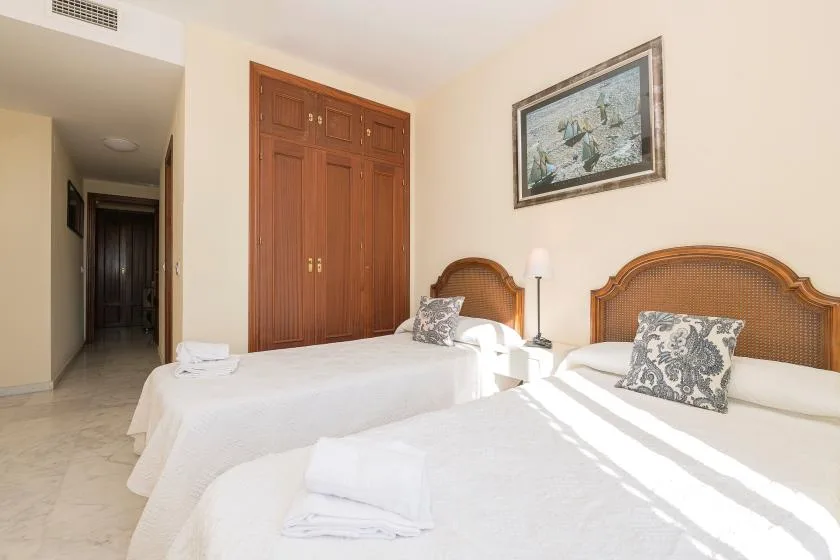 Un dormitorio con dos camas, ropa de cama blanca y un cuadro enmarcado en la pared.