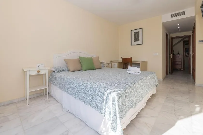 Un dormitorio con una cama tendida y una abertura hacia el pasillo.