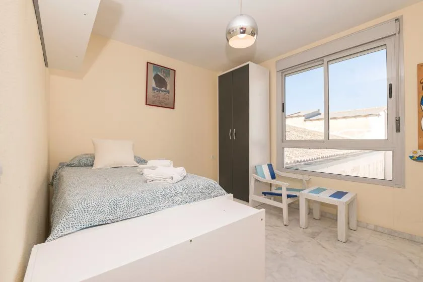 Un dormitorio con una cama, un armario y sillas junto a una ventana grande.
